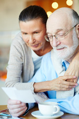 Obraz premium Senior man and woman having nostalgic time while looking through photos