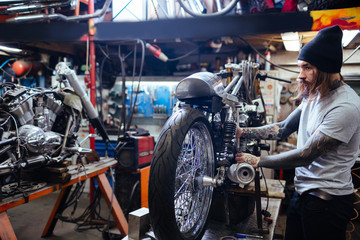 Fototapeta na wymiar Side view portrait of tattooed man working in garage repairing big motorcycle