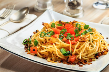 spaghetti with tomatoes, roasted garlic and green onions on a beautiful rectangular plate are on the table