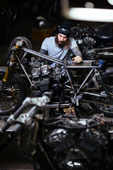 Portrait of modern heavily tattooed man assembling custom motorcycle in garage