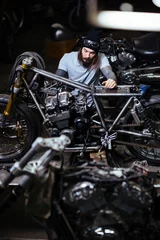 Acrylic prints Motorcycle Portrait of modern heavily tattooed man assembling custom motorcycle in garage