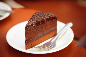 Pieces of delicious chocolate cake with fork on dish in coffee shop