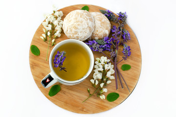 Herbal tea in a cup with a cookie on a wooden board. Decorated with wildflowers and acacia flowers. White background