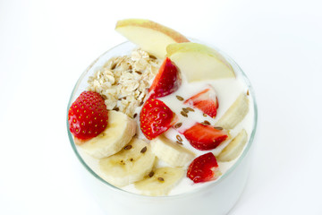 Glass of white yogurt with banana, oat flakes, strawberry, flax seeds on a white background close-up