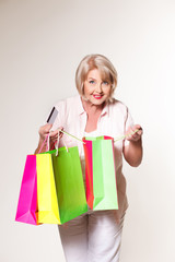 Fototapeta premium Elderly woman on a white background with shopping bags and a bank card