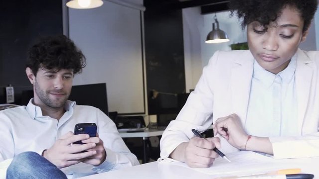 Man using mobile phone while colleagues do paperwork