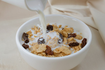 Pouring Milk In Bowl of Cereal and Raisin for Breakfast Meal.