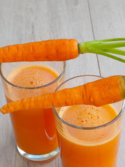 glass of fresh carrot juice with vegetables on wood background.