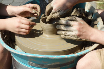 Teenager traditional artisan teaches younger boy how to mold clay on potter’s wheel