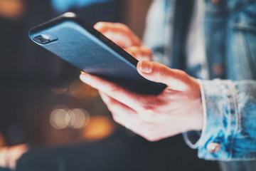 Closeup view of female hands holding modern smartphone and pointing fingers on the touch screen at night.Horizontal, blurred background, bokeh effects.
