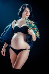 Beautiful pregnant woman on black studio background. Dressed in a black vest and black lingerie.