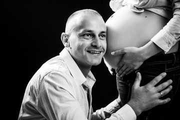 Handsome man is listening to his beautiful pregnant wife's tummy and smiling  black and white photo