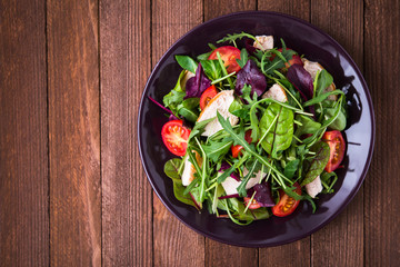 Fresh salad with chicken, tomatoes and mixed greens (arugula, mesclun, mache) on wooden background top view. Healthy food.