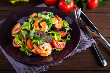 Fresh salad plate with shrimp, tomato and mixed greens (arugula, mesclun, mache) on wooden background close up. Healthy food. Clean eating.