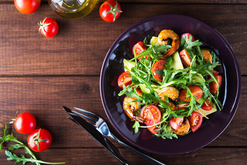 Fresh salad plate with shrimp, tomato, avocado and arugula (salad rocket) on wooden background top...