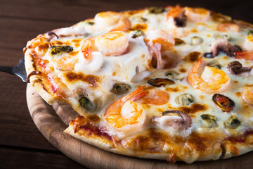 Slice of italian seafood pizza with shrimp, octopus, clams, mussels and squid on dark wooden background close up. Italian traditional food. Popular street food. Frutti di Mare pizza.