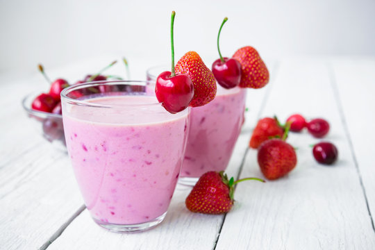 Cherry, blueberry, strawberry milkshake and tasty berries on white wooden table.