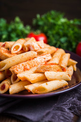 Penne pasta with tomato sauce on dark wooden background. Italian cuisine.