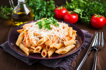 Penne pasta with chicken, tomato sauce, parmesan cheese and parsley on dark wooden background close up. Italian cuisine.