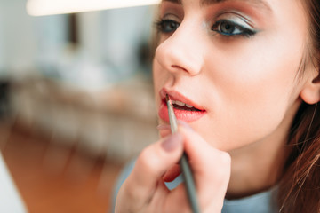 Make up artist hand applying gloss on woman lips