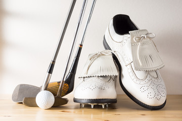 used white leather shoes, golf club and ball on pine wood floor against rustic wall