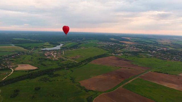 Red balloon in the shape of a heart.Aerial view:Hot air balloon in the sky over a field in the countryside, beautiful sky and sunset. Aerostat fly in the countryside. 4K video,ultra HD.