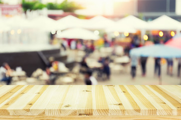 Blurred image of food fairs and food festivals consist of many booth and vendors at food stalls. People walking in street. Event in Chiang Mai at twilight montage with wood table top for background.