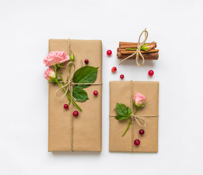 Gift box and envelope in eco paper on white background. Presents decorated with roses and berries. Holiday concept, top view, flat lay