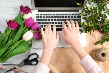 Photo sur Plexiglas Fleuriste Female florist with laptop and flowers on wooden table