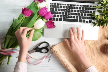 Fototapete Blumenladen Blumenhändlerin mit Laptop und Blumen auf Holztisch