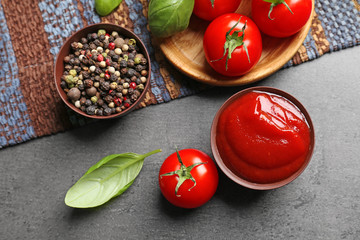 Delicious ketchup in bowl with ingredients on dark background, top view