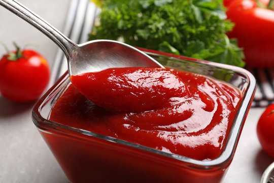 Delicious ketchup in bowl and spoon, closeup