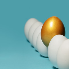 Concept of individuality, exclusivity, better choice. One golden egg among white eggs on blue...