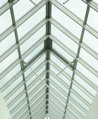 A view through a triangular arched glass roof to the overcast sky, white aluminum frames, double-glazed windows. Photo partially toned 