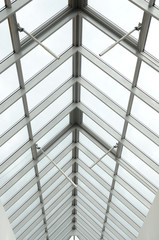 A view through a triangular arched glass roof to the overcast sky, white aluminum frames, double-glazed windows. Photo partially toned 