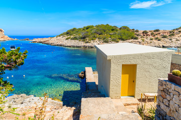 Small house with yellow door on sea coast and view of Cala Portinatx bay, Ibiza island, Spain