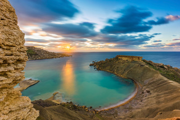 Mgarr, Malta - Panorama of Gnejna bay, the most beautiful beach in Malta at sunset with beautiful colorful sky and golden rocks taken from Ta Lippija - obrazy, fototapety, plakaty