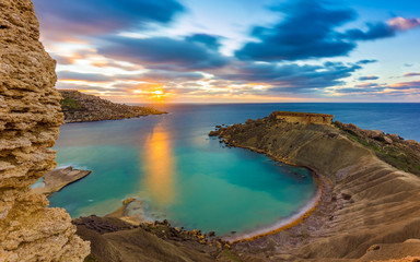 Mgarr, Malta - Panorama of Gnejna bay, the most beautiful beach in Malta at sunset with beautiful colorful sky and golden rocks taken from Ta Lippija