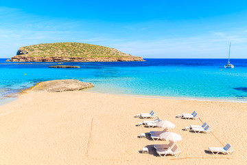 View of beautiful Cala Comte beach with sunbeds and umbrellas - famous for its azure crystal clear shallow sea water, Ibiza island, Spain