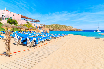 Wooden walkway on sandy Cala Comte beach and restaurant building on shore, Ibiza island, Spain.