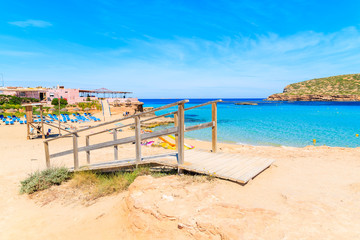 Wooden walkway on sandy Cala Comte beach and restaurant building on shore, Ibiza island, Spain.