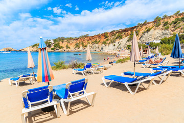 View of Cala d'Hort beach with sunbeds and umbrellas and beautiful azure blue sea water, Ibiza...