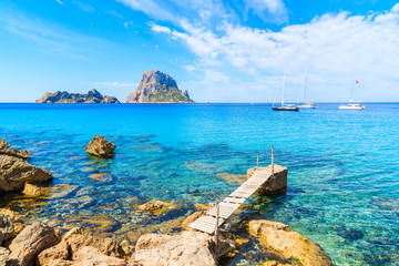 Small wooden pier in Cala d'Hort bay and view of Es Vedra island, Ibiza island, Spain - obrazy, fototapety, plakaty