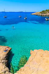 Fototapeta na wymiar Unidentified man tourist sunbathing on a rock in Cala Salada bay with beautiful sea cove, Ibiza island, Spain