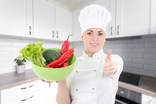 young cook woman in uniform with vegetarian food thumbs up in modern kitchen