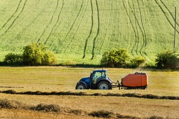 Blue tractor collects dry hay. Agricultural work on the farm in the Czech Republic.