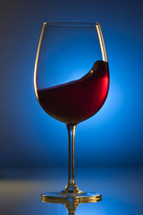 Red wine in a glass. A single glass. Colorful background. Wine-making. Reflection from a glossy surface.
