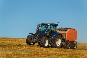 Blue tractor collects dry hay. Agricultural work on the farm in the Czech Republic.
