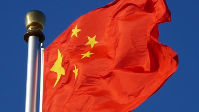 Chinese red flag flutters in wind & blue sky.