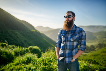 bearded guy with sunglasses and blue flannel posing in front of grassy green hills in california - obrazy, fototapety, plakaty